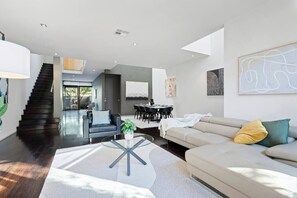 A modern living room with a staircase, a dining area, and a sofa with cushions. - Sia - Ultimate Executive Home with 4BDR and Parking (South Yarra)
