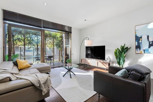 A modern living room with a sofa, a coffee table, a TV, and a dining area. - Sia - Ultimate Executive Home with 4BDR and Parking (South Yarra)
