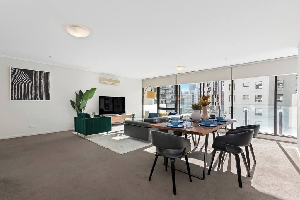 A modern living room with a dining area, large windows, and a flat-screen TV.