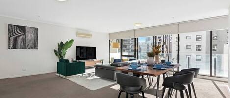 A modern living room with a dining area, large windows, and a flat-screen TV.