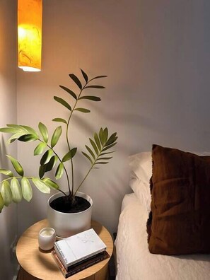 Ein Schlafzimmer mit Nachttisch, Topfpflanze, Buch und Kissen.