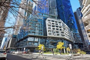 A modern building with a glass facade, surrounded by other high-rise structures. - Xia -Jaw-dropping 3BD2BTH Executive City Residence (Melbourne)