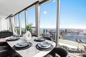Ein Essbereich mit Tisch für vier Personen, großen Fenstern und Blick auf Stadt und Fluss.