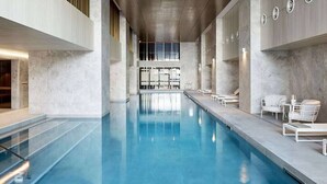 Una piscina con vista despejada al techo y las paredes, un área de descanso con sillas, y un ventanal que proporciona luz natural.