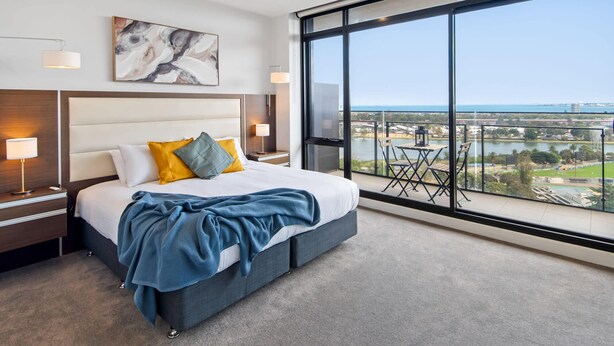 A modern hotel room with a large bed, a view of the city, and a balcony with outdoor seating. - Jaw-dropping Views from 3bdr Executive Penthouse (Melbourne)