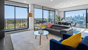 A modern living room with large windows, a sofa, a coffee table, and a city view. - Jaw-dropping Views from 3bdr Executive Penthouse (Melbourne)