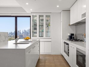 Eine moderne Küche mit Stadtblick, weißen Schränken, einer großen Kochinsel mit Spüle und einem eingebauten Backofen.