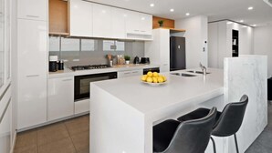 A modern kitchen with white cabinetry, a central island with chairs, a stove, and a sink. - Jaw-dropping Views from 3bdr Executive Penthouse (Melbourne)