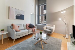 A modern living room with a grey sofa, a round glass coffee table, a side table with a plant, a floor lamp, and a large window. - Famous Degraves Lane Stunner with Parking! (Melbourne)