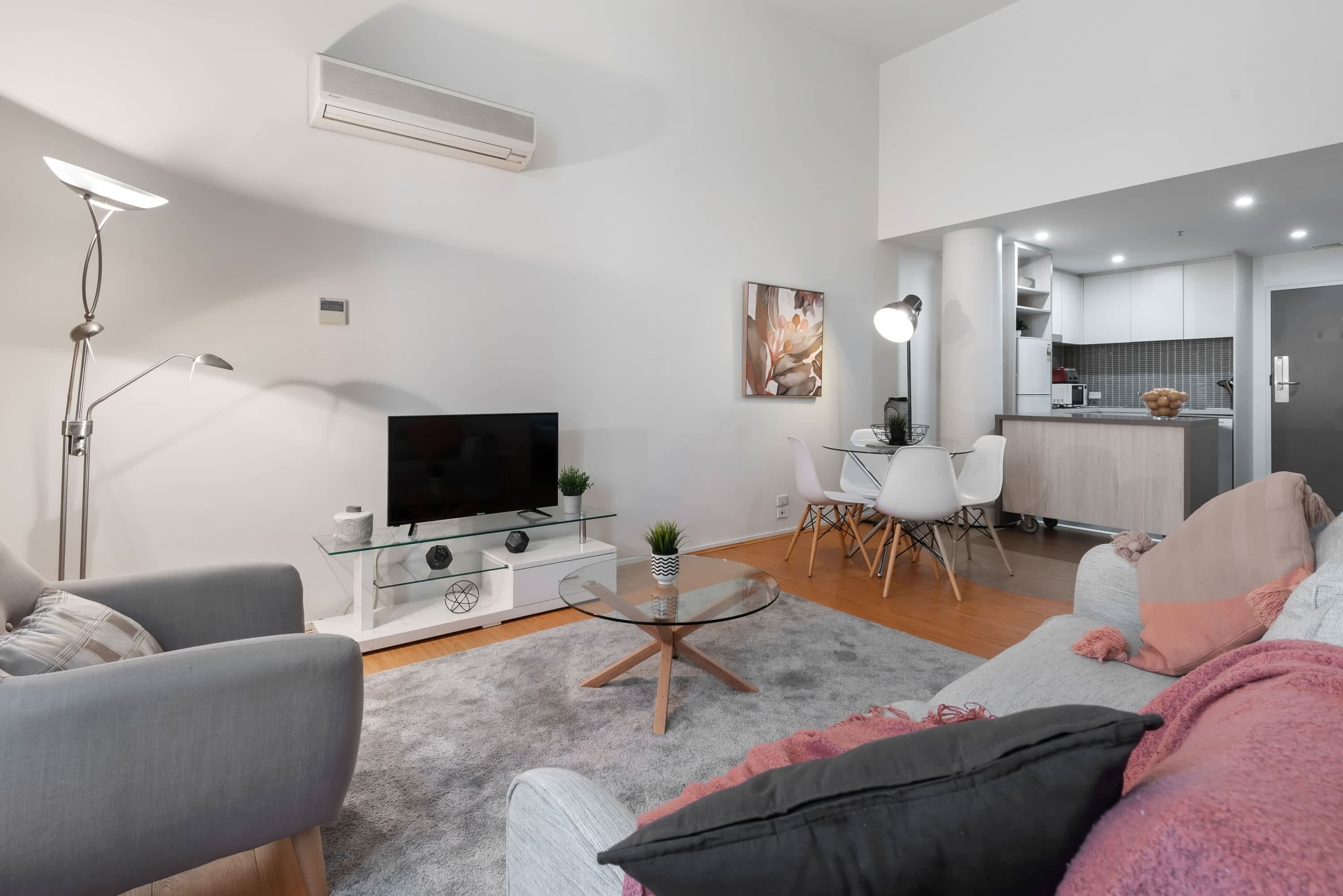 Uma sala de estar moderna com televisão de tela plana, mesa de centro de vidro e um sofá.