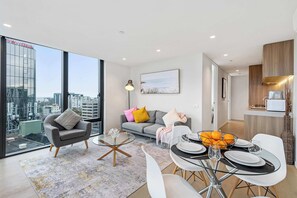 Ein modernes Wohnzimmer mit Glastisch, einer Couch mit bunten Kissen und einem Essbereich mit weißem Tisch und gedecktem Tisch.
