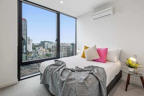 Ein Schlafzimmer mit großem Fenster, einem Bett, einem Nachttisch mit Lampe und einer Klimaanlage.