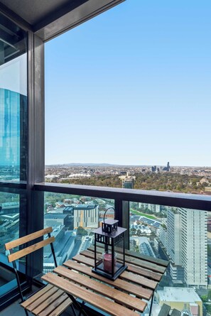 Ein Balkon mit einer Holzbank und einem Tisch, mit Blick auf eine Stadtlandschaft aus Gebäuden und einem klaren Himmel.