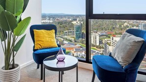 A modern room with a large window, two blue chairs, a small table, and a potted plant. - Resort-style 3bed2bath Executive Southbank Pad (Southbank)