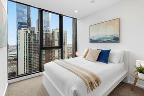 A bedroom with a large window, a bed, a painting, and a small table with a plant. - Executive 3BD City Haven with Parking + Views (Melbourne)