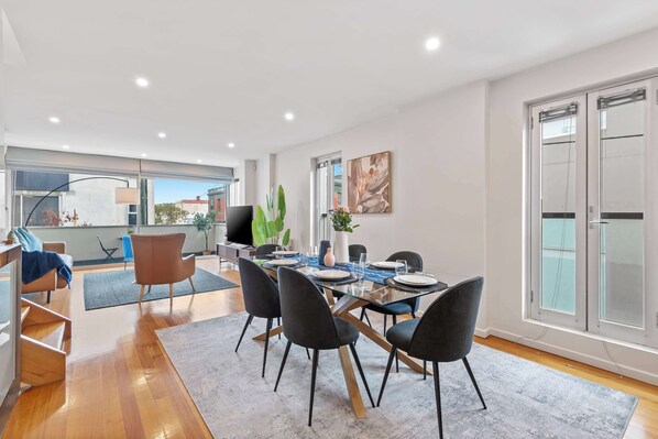 A modern dining area with a glass table, black chairs, and a view of the city.