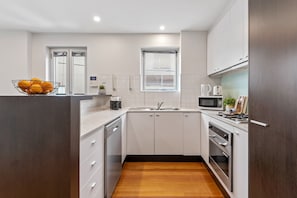 A compact kitchen with white cabinets, a microwave, a sink, and a wooden floor.