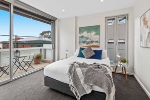 A modern bedroom with a large bed, a balcony with outdoor furniture, and a painting on the wall.