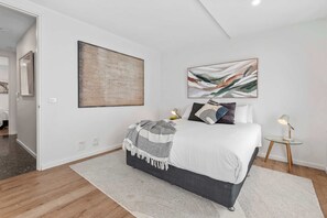 A bedroom with a bed, a bedside table with a lamp, and two wall-mounted artworks.