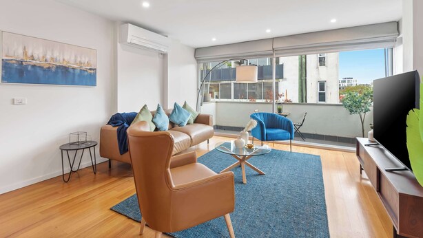 Ein modernes Wohnzimmer mit einem Ledersofa, einem blauen Sessel, einem Couchtisch und einem Fernseher auf einem Holzgestell.