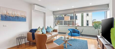 Uma sala de estar moderna com um sofá de couro, uma poltrona azul, uma mesa de centro e uma TV em um suporte de madeira.