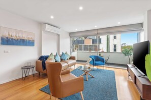 A modern living room with a leather sofa, a blue armchair, a coffee table, and a TV on a wooden stand.