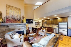 A spacious living room with a fireplace, a kitchen with wooden cabinets, and a dining area. - Ski-in/out Mountain view condo w/fast WiFi, fireplace, shared pool/hot tubs/WD (Vail)