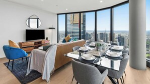 Een moderne woonkamer met een eethoek, een flatscreen televisie, een bank en een groot raam met uitzicht op de stad.