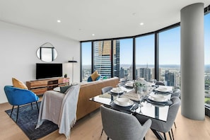 Ein modernes Wohnzimmer mit Essbereich, einem Flachbildfernseher, einer Couch und einem großen Fenster mit Blick auf die Stadt.