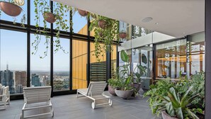 Een moderne lounge met grote ramen, plantenpotten en witte fauteuils.