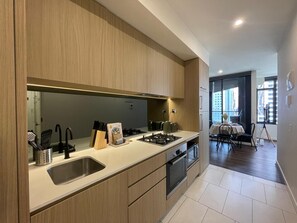 A modern kitchen with wooden cabinets, a stainless steel sink, and a dining area with a table and chairs. - Stunning, spacious, chic and central city pad (Melbourne)