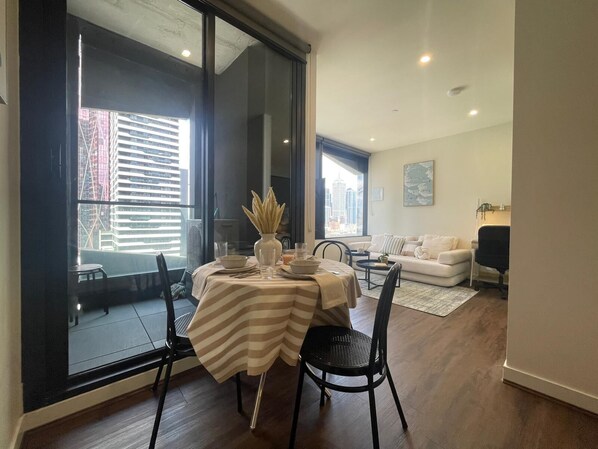 A dining area with a table set for two, a sofa, and a large window with a city view. - Stunning, spacious, chic and central city pad (Melbourne)
