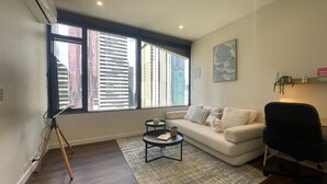 Een moderne woonkamer met een witte bank, een zwarte bureaustoel, een klein rond tafeltje en een statief.