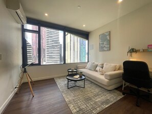 A modern living room with a white sofa, a black office chair, a small round table, and a tripod stand. - Stunning, spacious, chic and central city pad (Melbourne)