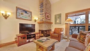 A living room with a fireplace, a television, a sofa, and a coffee table. - Elegant, ski-in/out condo w/ fireplace, fast WiFi, shared pool/hot tubs/laundry (Vail)