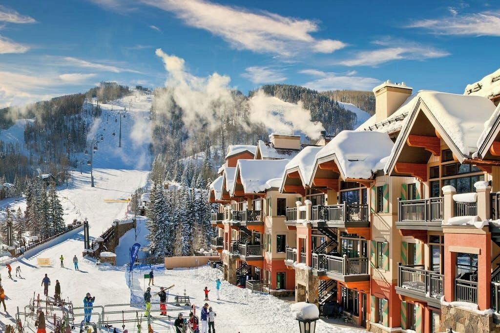 Ein Skigebiet mit mehrstöckigen Gebäuden, einer Skipiste und einem verschneiten Berg im Hintergrund.