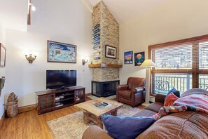 Ein Wohnzimmer mit Kamin, Fernseher, Ledersessel und großem Fenster.