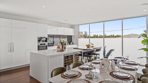 Cozinha moderna com armários brancos, área de jantar com mesa grande posta para seis pessoas e vista para a cidade através de amplas janelas.