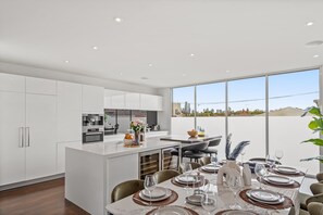 Eine moderne Küche mit weißen Schränken, ein Essbereich mit einem großen Tisch für sechs Personen und Blick auf die Stadt durch große Fenster.