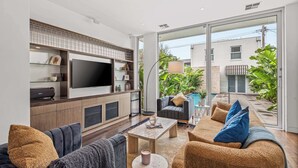 Uma sala de estar moderna com televisão de tela plana, sofá, mesa de centro e vista para uma piscina e vegetação.