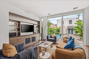 Ein modernes Wohnzimmer mit Flachbildfernseher, Sofa, Couchtisch und Blick auf einen Pool und Grünflächen.