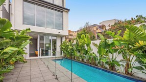 Um edifício moderno com piscina, rodeado por plantas tropicais.