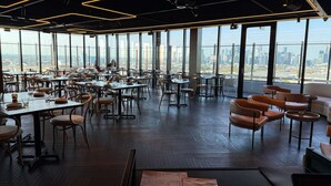A spacious dining area with high ceilings, modern lighting, and large windows offering a city view. - Executive apt. +views +parking in beachside resort (Port Melbourne)