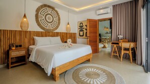 A modern bedroom with a wooden headboard, a large bed, a round woven rug, a dining area with a table and chairs, and a wall-mounted air conditioner. - Infinity Pool Villa with Jungle & River View (Tabanan)