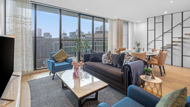 A modern living room with a sofa, chairs, a coffee table, and a dining area. - Luxe Docklands Townhouse with 2 Carspaces +Views! (Docklands)
