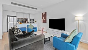 A modern living room with a sofa, a coffee table, a TV, and a lamp. - Luxe Docklands Townhouse with 2 Carspaces +Views! (Docklands)