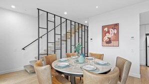 A modern dining area with a round table, six chairs, and a staircase with glass railings. - Luxe Docklands Townhouse with 2 Carspaces +Views! (Docklands)