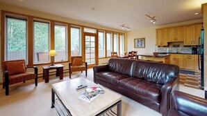 A spacious living room with a leather sofa, a coffee table, and a dining area with a table and chairs. Large windows provide ample natural light. - Bright Mountain Retreat w/Shared Pool & Hot Tub & Mountain Views from Balcony (Vail)