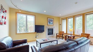 A living room with a fireplace, a television, leather sofas, and large windows. - Bright Mountain Retreat w/Shared Pool & Hot Tub & Mountain Views from Balcony (Vail)