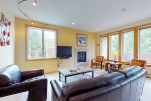A living room with a fireplace, a television, leather sofas, and large windows. - Bright Mountain Retreat w/Shared Pool & Hot Tub & Mountain Views from Balcony (Vail)